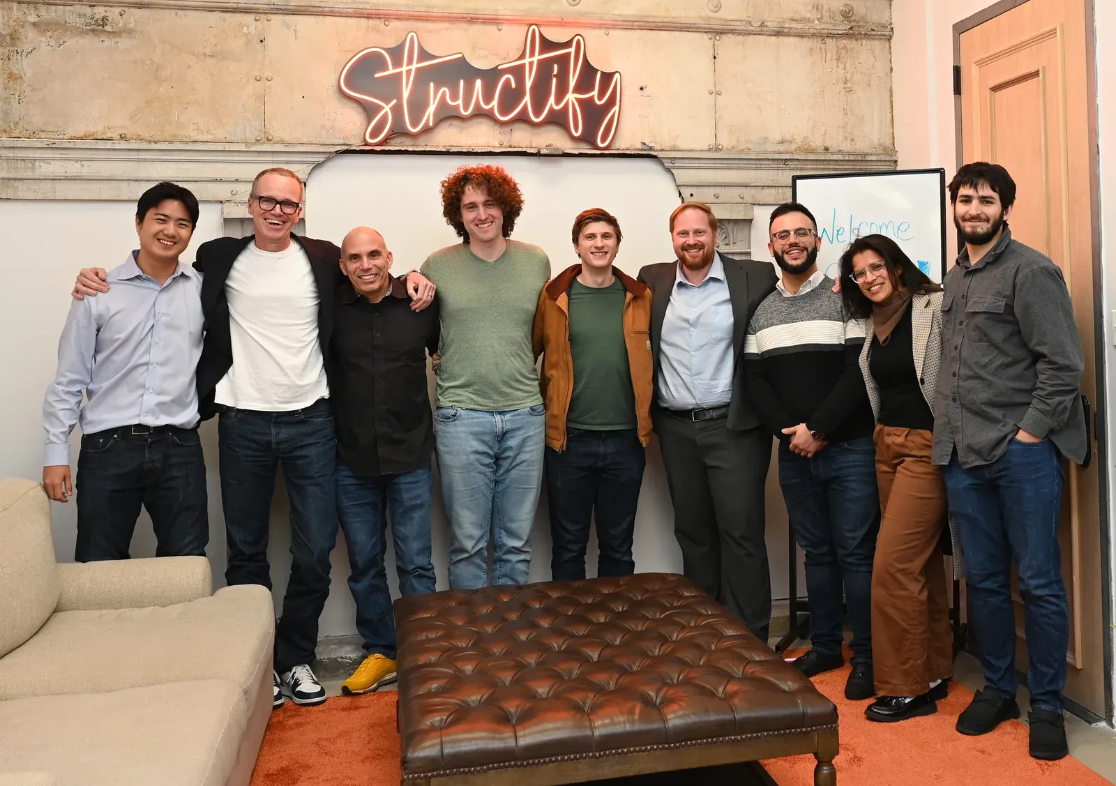 The Structify team standing together under the neon sign in the Brooklyn office